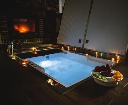 Foto del jacuzzi en el suelo con la chimenea junto a un lado, una botella de cava y las luces azules encendidas.