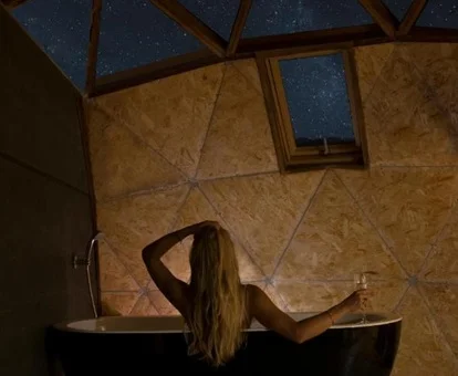 Mujer disfrutando dentro de una bañera tomanto una copa de cava mientras ve las estrellas a través del techo acristalado