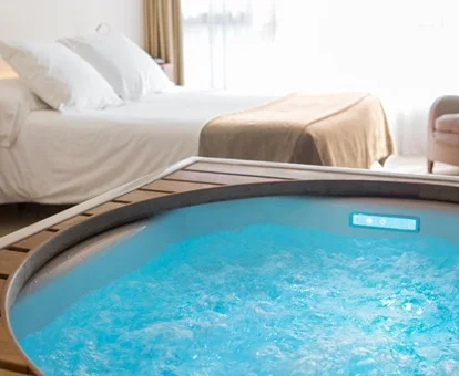 Foto del jacuzzi lleno y con luz turquesa que se encuentra frente a la cama en la suite deluxe con bañera de hidromasaje en Hotel Diagonal Zero de Barcelona