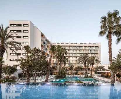 Edificio del hotel con grandes piscinas rodeadas de palmeras.