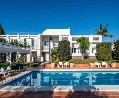Precioso hotel con bellos jardines y piscina al aire libre con tumbonas.
