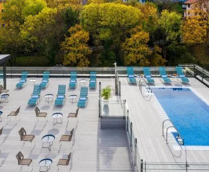 Piscina exterior con solarium de este hotel rodeada de árboles.