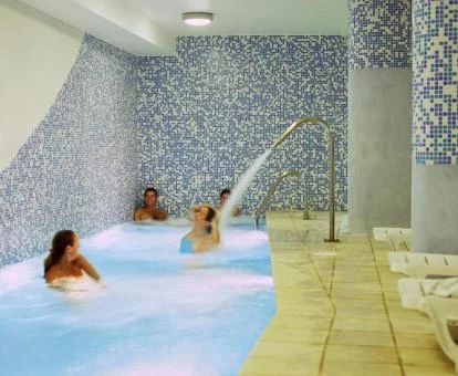 Varias personas disfrutando de la piscina cubierta con chorros del spa.