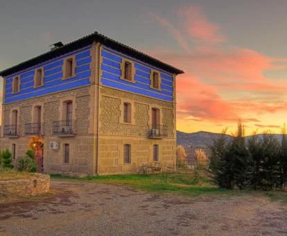 Edificio de este hotel rural rodeado de naturaleza con una bella puesta de sol al fondo.