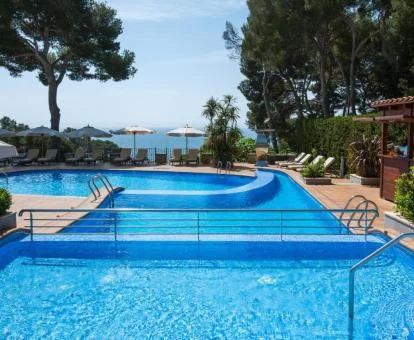Zona exterior del hotel rodeada de jardines con piscinas, vistas al mar y tumbonas.