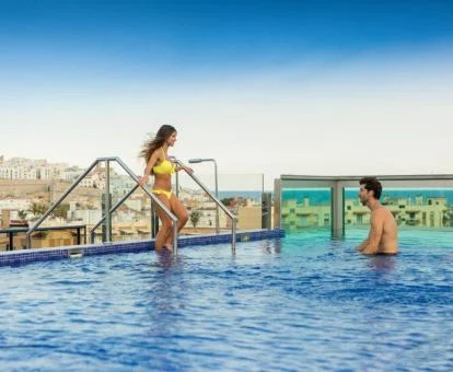 Pareja disfrutando de la piscina con preciosas vistas y zona de cristal del hotel.