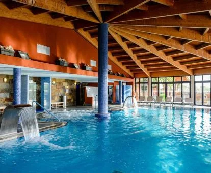 Gran piscina cubierta con elementos de hidroterapia y vistas al exterior del spa del hotel.