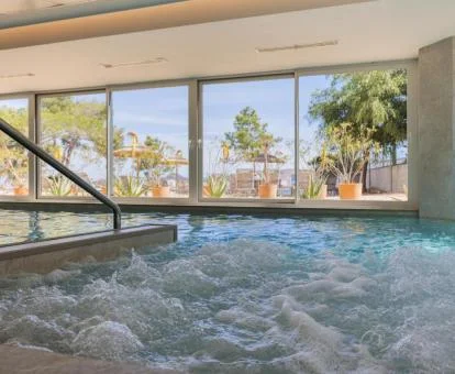 Piscina cubierta con elementos de hidroterapia en funcionamiento y vistas al exterior.