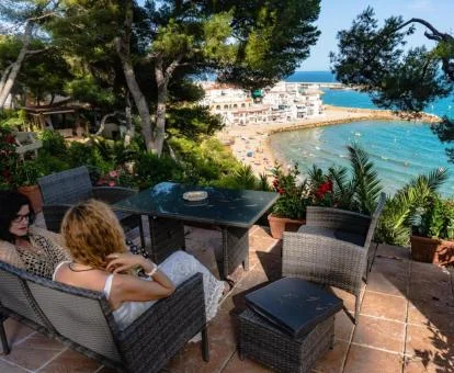 Dos mujeres disfrutando de la preciosa terraza con vistas al mar y rodeada de jardines de este alojamiento.