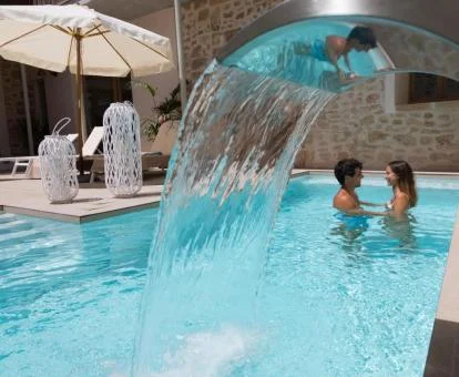 Pareja disfrutando de la piscina exterior con chorros en cascada de este hotel.