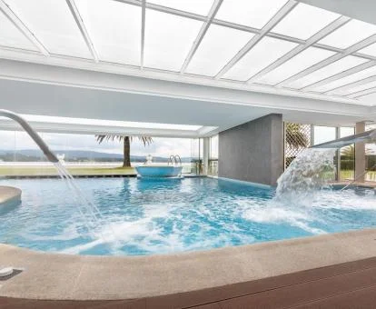 Gran piscina interior con elementos de hidroterapia y vistas al exterior del spa.