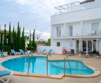 Piscina exterior con solarium y tumbonas junto a la fachada del hotel.