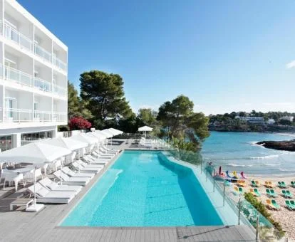 Maravilloso hotel con piscina exterior y tumbonas junto al mar.