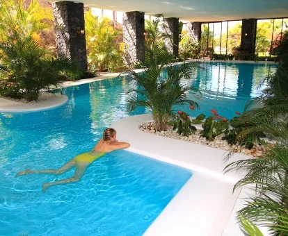 Mujer disfrutando de la preciosa piscina interior del spa rodeada de jardines.