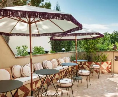 Encantadora terraza con largo sillón de obra, mesas, sillas y sombrillas para disfrutar al aire libre.