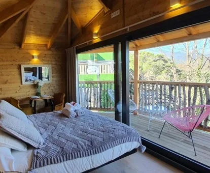Foto de la suite de la cabaña con suelo y paredes de madera donde se puede ver la cama, las cristaleras y los árboles a travás de la ventana