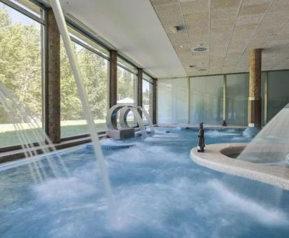 Piscina interior con hidroterapia del spa del hotel con vistas al exterior.
