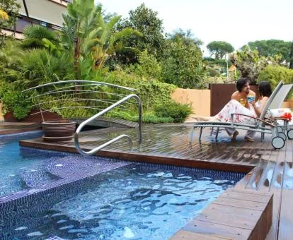 Pareja relajándose en las tumbonas de la piscina de este hotel con hermosos jardines.