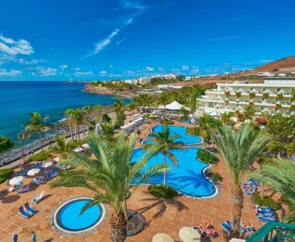 Precioso hotel solo para adultos junto al mar con piscinas, solarium con tumbonas y jardines con palmeras.