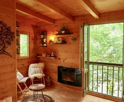foto del interior de madera con chimenea, la cama y un balcón con vistas a los árboles sobre los que se encuentra.
