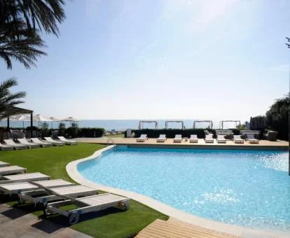 Amplia piscina exterior con solarium y vistas al mar del hotel.