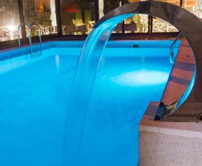 Piscina cubierta con elementos de hidroterapia y vistas al exterior del spa.