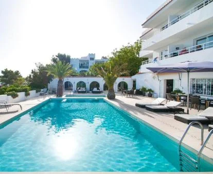 Fachada de este precioso hotel con amplia piscina exterior con tumbonas y palmeras.