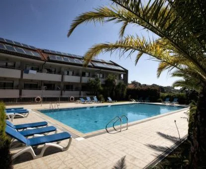 Edificio de este hotel solo para adultos con piscina exterior y solarium con tumbonas rodeados de palmeras.