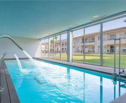 Piscina interior con chorros y vistas al jardín.